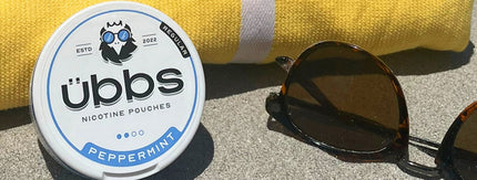 übbs Peppermint nicotine pouch can leaning against beach towel with sunglasses