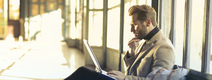 a man in a sunny corridor looking quizzical at a laptop