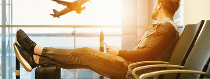 man reclining in airport chair with legs on suitcase, plane taking off in background